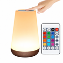 Luminária de mesa acesa e controle remoto em fundo branco, com mão sobre o sensor de toque